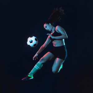 Young woman kicking a football while in the air