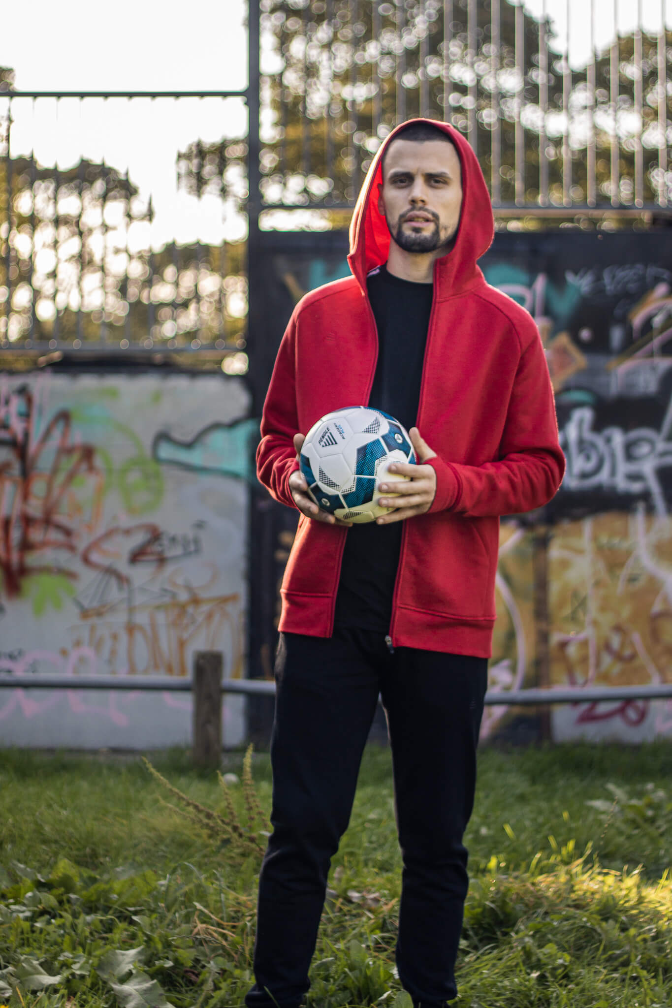Model wearing a red hoodie, black joggers and a black t-shirt from Pendle Sportswear. He is holding a Pendle football.
