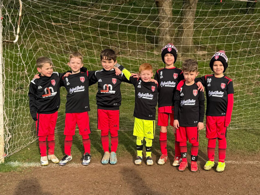 A team of young players wearing sweatshirts and hats over their football kits.