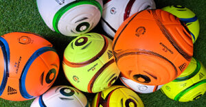 A photo of yellow, white and orange match and training footballs in a pile