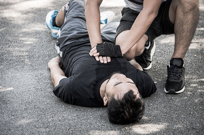 There is a man laid on the ground with another man crouched beside him, giving him CPR.