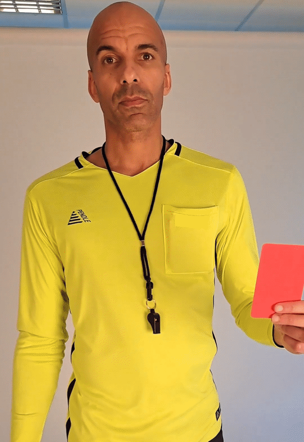 Man in a reversible goalkeeper shirt. He's wearing a fluo yellow shirt at the start then covers the camera with a red card and is wearing the reverse- a black shirt. He is wearing a referees whistle round his neck also.