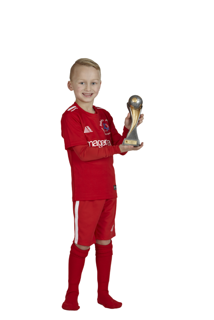 A young child wearing a football kit and holding a trophy